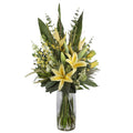 Yellow Lily and Heliconia Luminous Artificial Arrangement with soft yellow asiatic lilies, heliconia spikes, white globe thistle, green hypericum berries, and tropical foliage in a tall glass cylinder vase